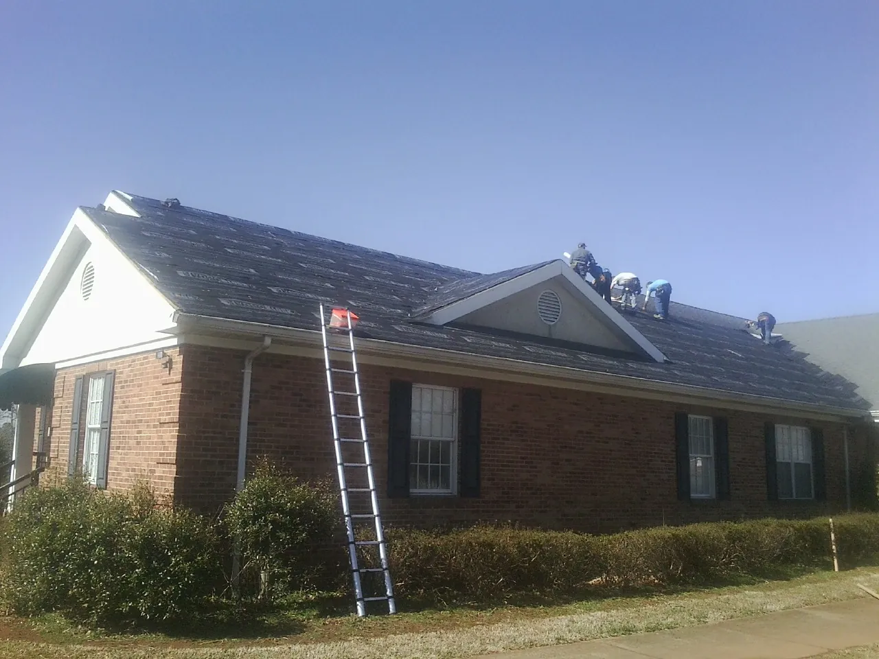 Crew tearing shingles off a brick ranch roof with a ladder set — Emergency Roof Repair work by our crew in Lucas