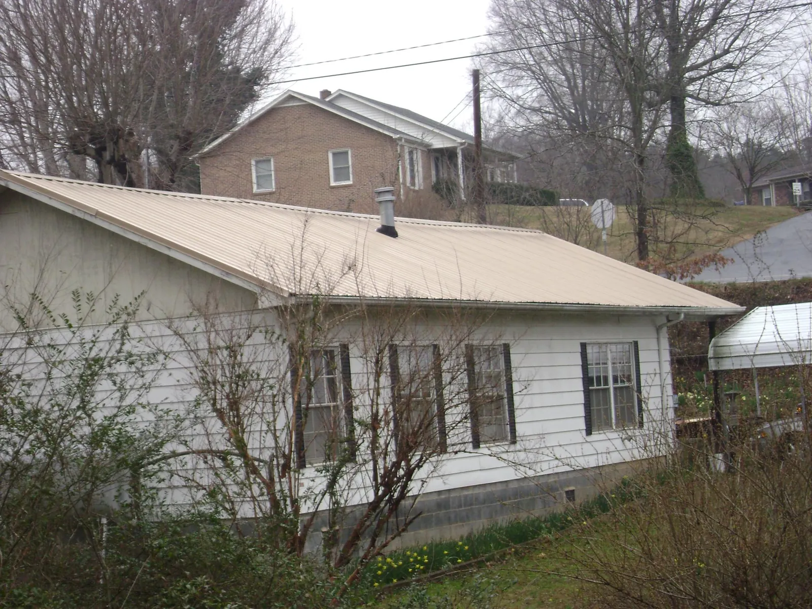 Tan metal roof on a white sided house set into a hillside — Commercial Roofing by Roofing Brothers in Lucas